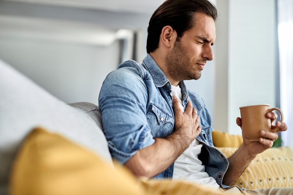 Man clutching chest and grimacing on couch, symbolizing systemic issues related to oral health at Toothbar in Austin, TX