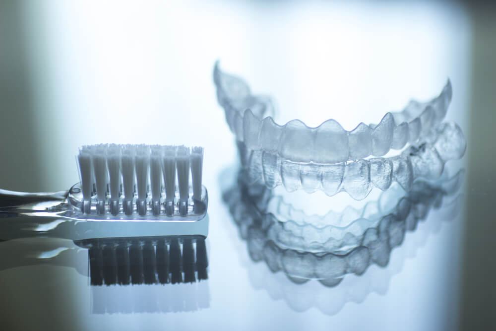 Invisalign sitting next to toothbrush on reflective surface