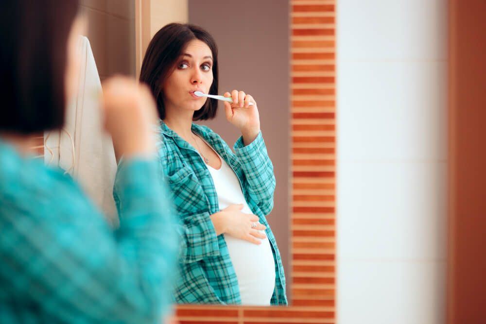 Pregnant woman brushing her teeth in mirror