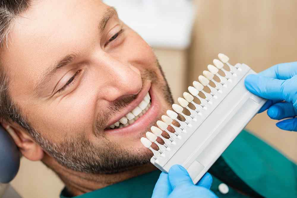 Man getting checked by the dentist testing different colors of porcelain veneers