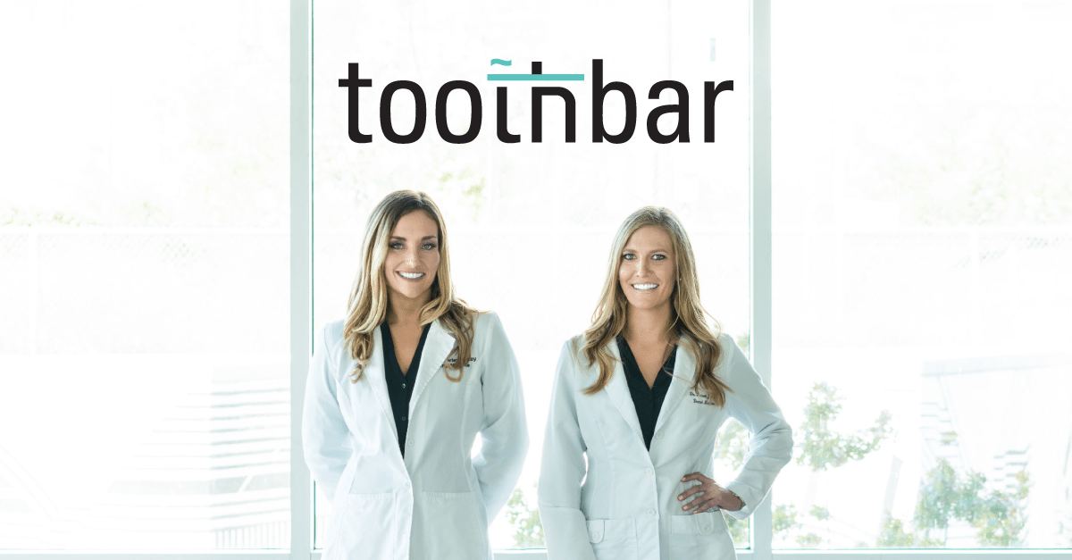 An image of both doctors standing in doctor jackets in front of a floor to ceiling window in the Toothbar Austin dental practice.