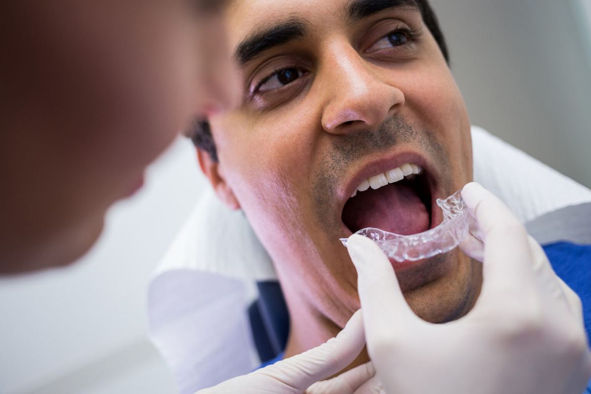 Dentist inserting a clear Invisalign aligner into a patient’s mouth, illustrating the application process on a page discussing the comfort of Invisalign treatments.