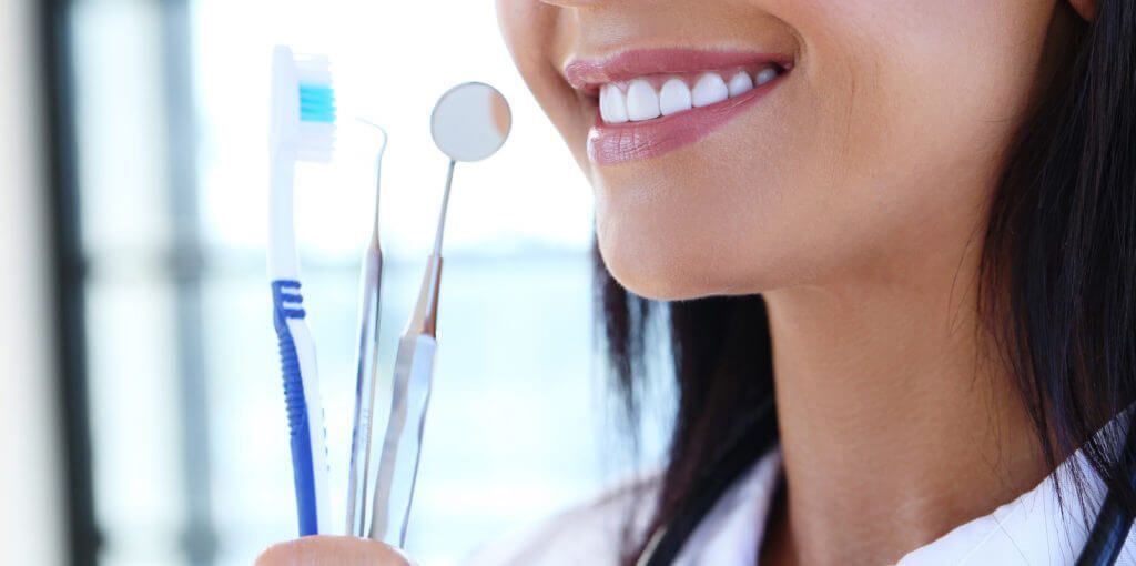 Dentist holding toothbrush, dental explorer, and dental mirror