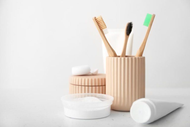 Toothbrushes in wooden cup sitting next to tube of toothpaste