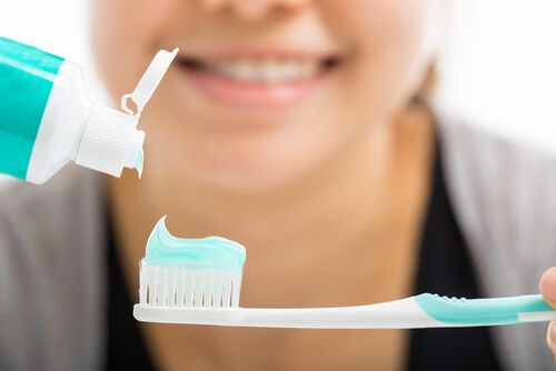 Happy person adding tooth paste to her toothbrush in order to brush teeth