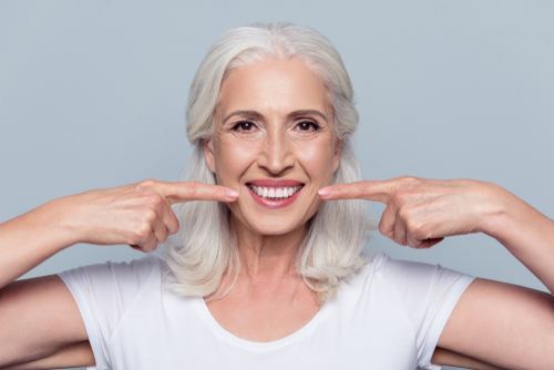 Senior woman in white shirt pointing to her smile