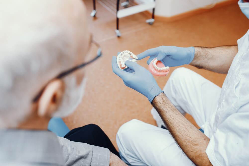 Dentist showing senior male patient model of teeth