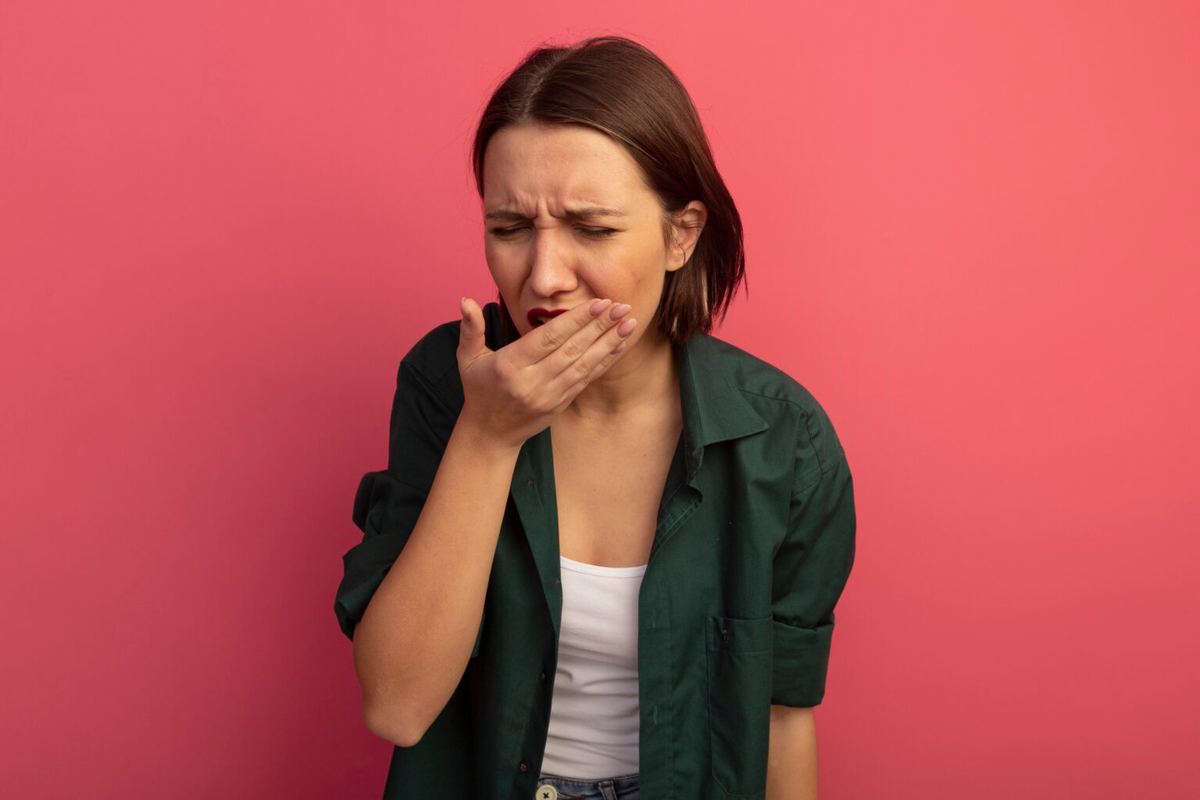 Woman holding her mouth in pain, set against a salmon-colored background, expressing acute dental discomfort.
