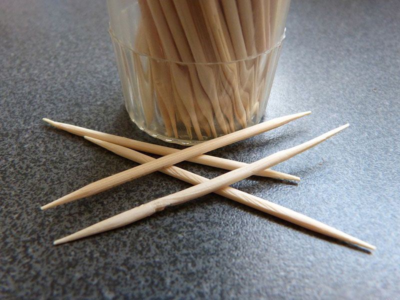 Toothpicks sitting on table in front of cup of toothpicks