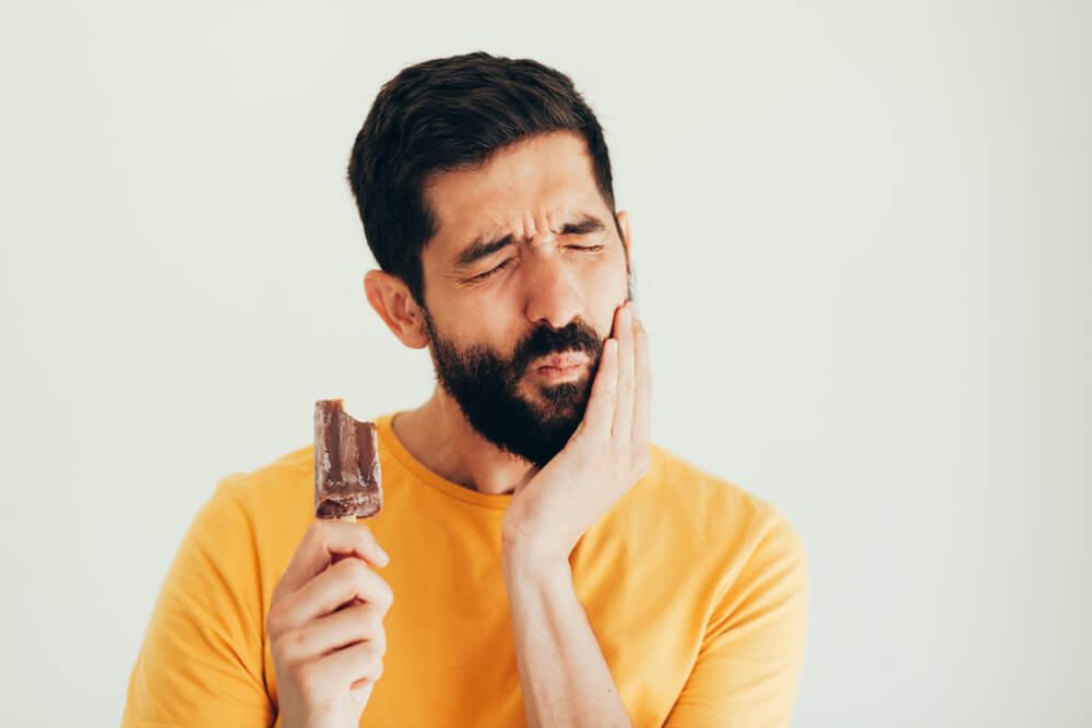 Man rubbing jaw in pain after taking bite of ice cream bar