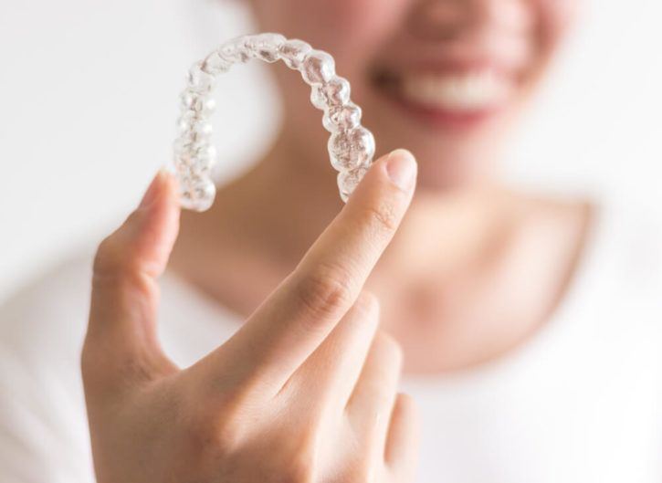 Person in white shirt holding a clear aligner