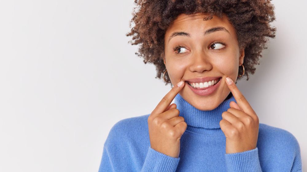 Woman in blue sweater pointing to her bright smile at Toothbar in Austin, TX