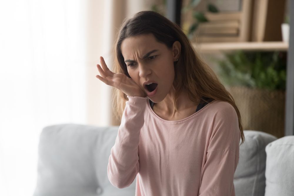 Woman in pink shirt sitting on couch and rubbing jaw