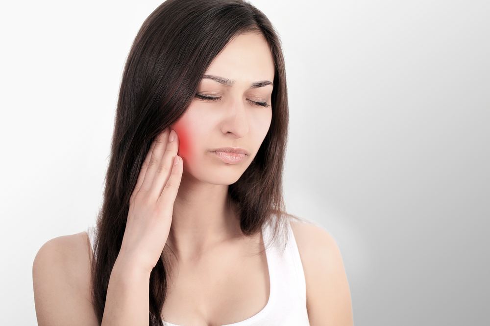 Woman in white shirt rubbing jaw in pain
