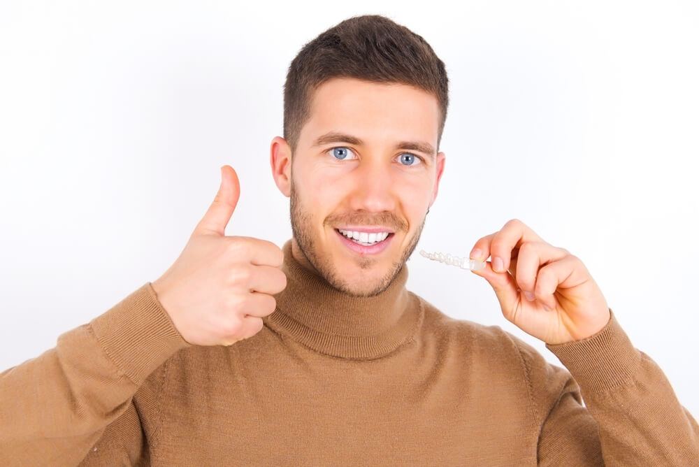 Man holding his invisalign aligner while smiling and giving a thumbs up on the other hand