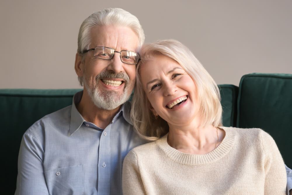 Senior man and woman sitting on couch smiling