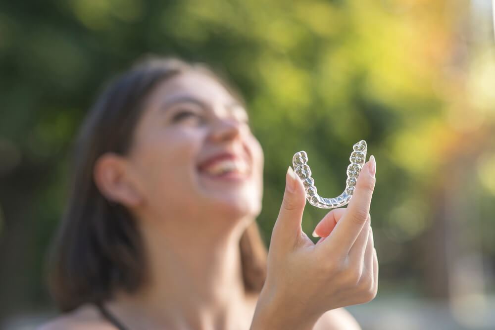 Woman outside laughing and holding Invisalign aligner