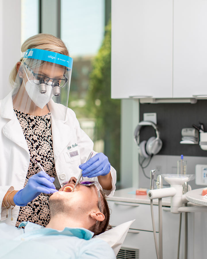 A Toothbar dentist wearing a face shield and loupes examining a patient's teeth