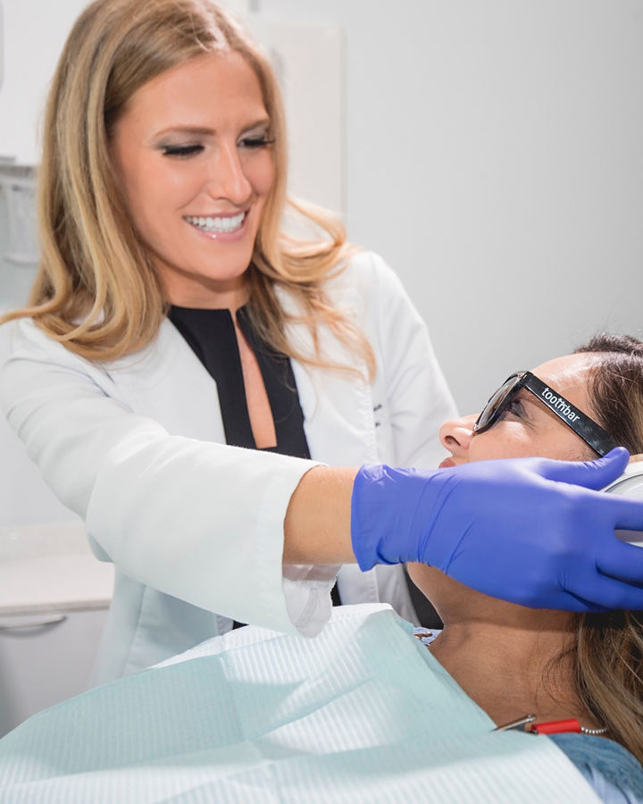 A dentist gently settling noise-canceling headphones on a reclined patient before treatment