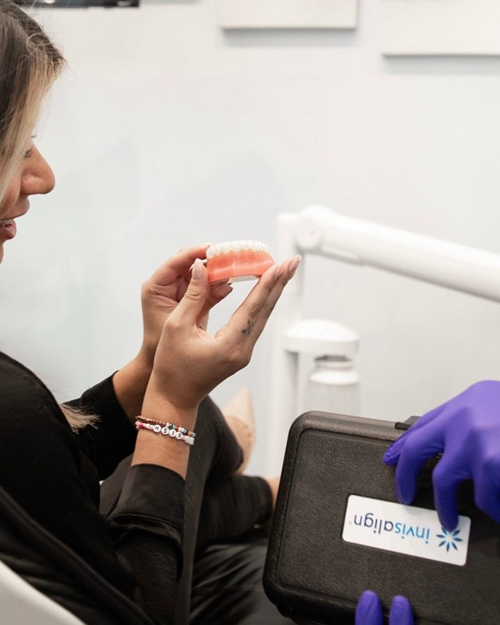 Gloved hands handing a patient her clear aligners next to an Invisalign case