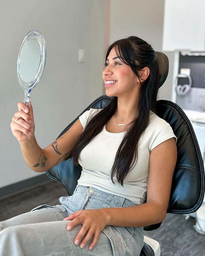 A patient smiling at her reflection in a hand mirror, seated in a Toothbar dental chair
