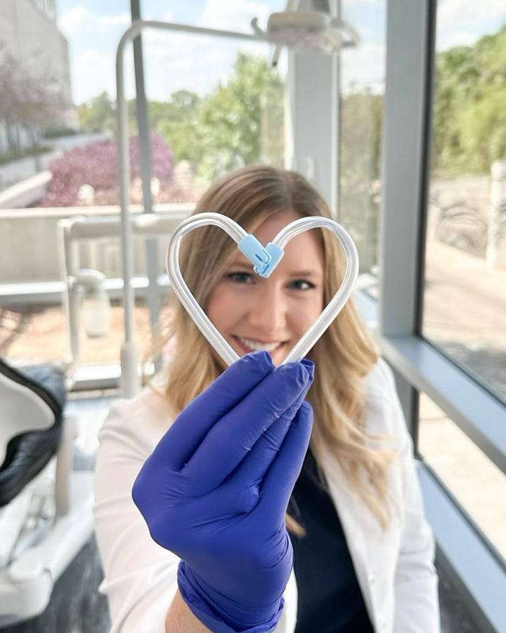 A dentist holding up a heart shaped from dental floss with a gloved hand