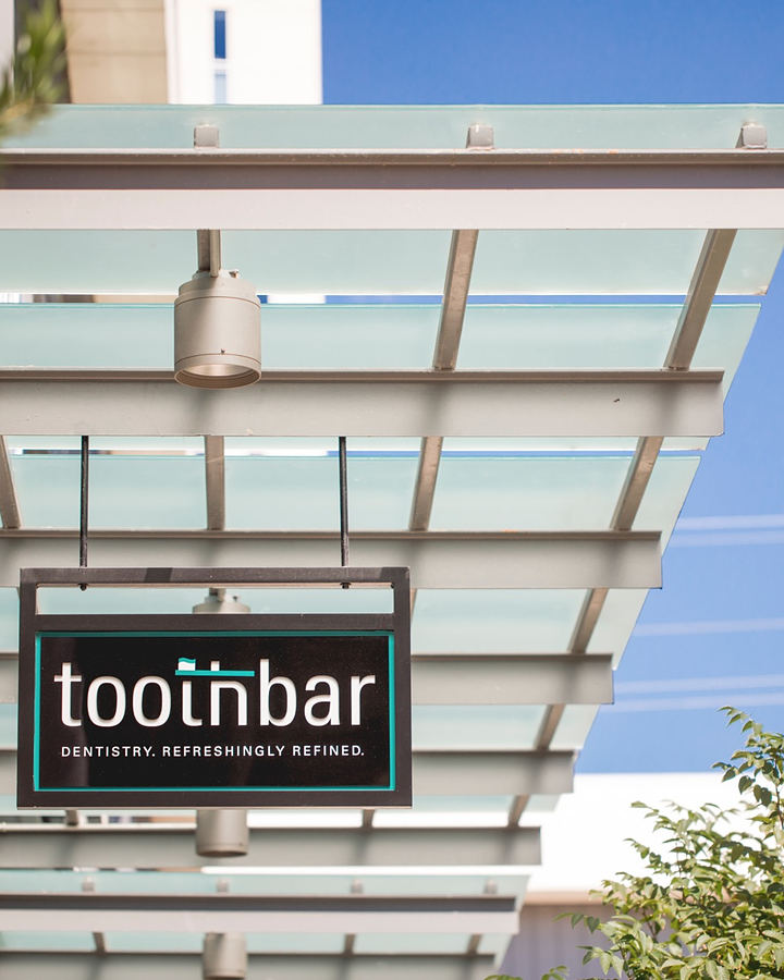 The Toothbar sign, reading Dentistry. Refreshingly refined., hanging under a glass canopy against a blue sky