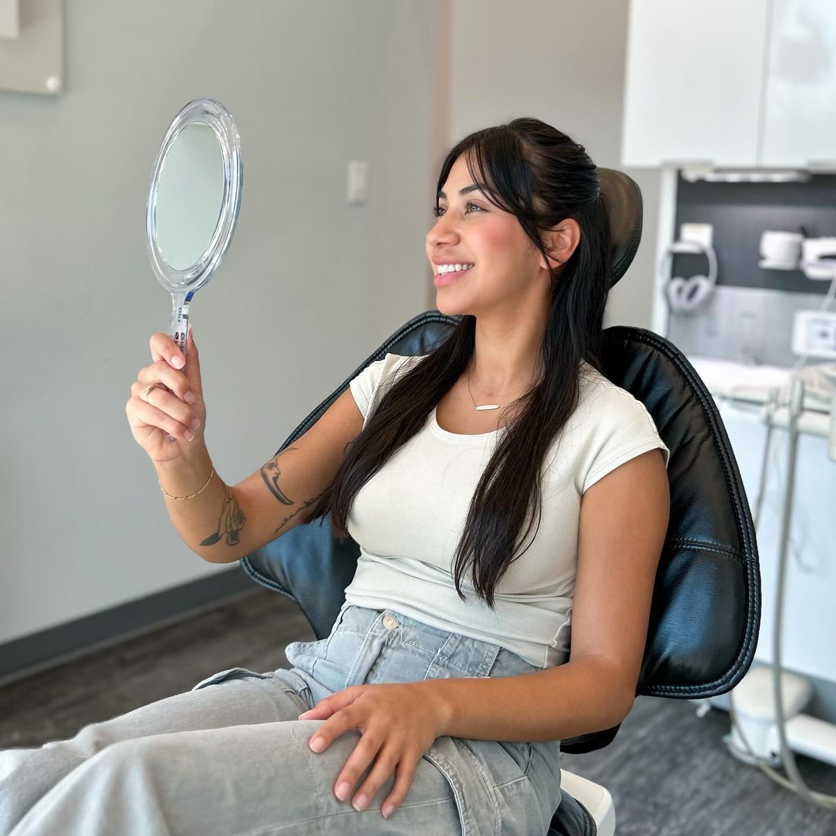 Woman sitting in dental chair checking smile in mirror